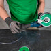 Person using a diamond grinding machine on a black surface with a green shirt and gloves.